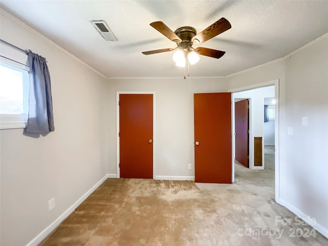 unfurnished bedroom featuring ceiling fan, light colored carpet, a textured ceiling, and ornamental molding