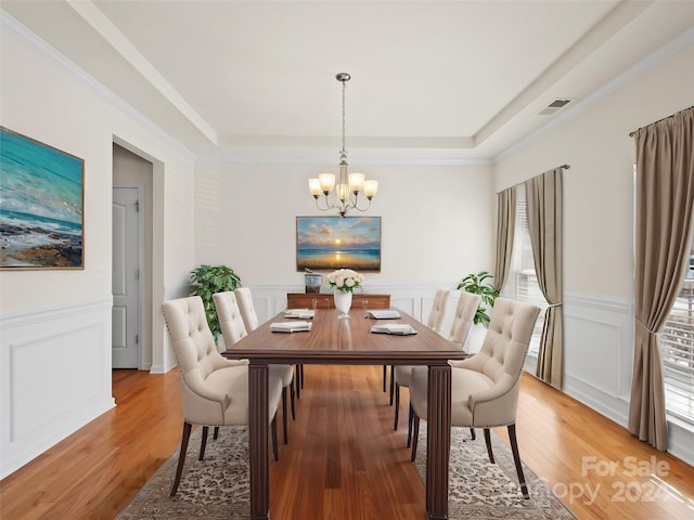 dining area with a raised ceiling, wood-type flooring, an inviting chandelier, and ornamental molding