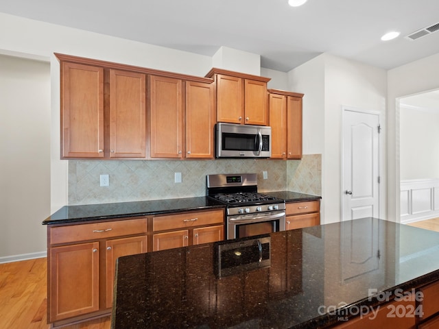 kitchen featuring dark stone countertops, backsplash, appliances with stainless steel finishes, and light wood-type flooring