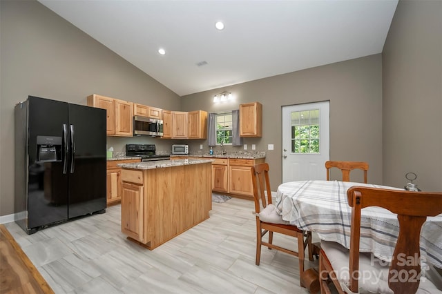 kitchen featuring light stone counters, black appliances, light brown cabinets, a center island, and lofted ceiling