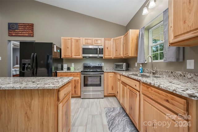 kitchen featuring appliances with stainless steel finishes, light brown cabinetry, light stone counters, vaulted ceiling, and sink