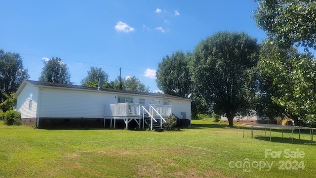 rear view of property with a trampoline, a lawn, and a deck