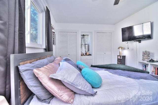 bedroom with lofted ceiling, ornamental molding, two closets, and ceiling fan