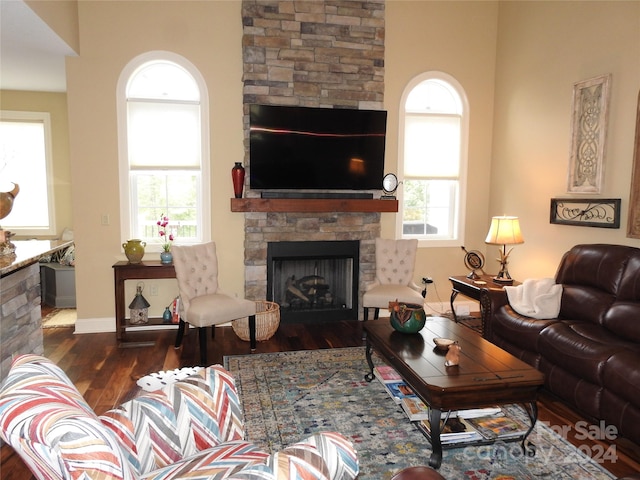 living room with a wealth of natural light, dark wood-type flooring, and a stone fireplace