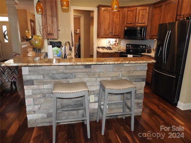 kitchen featuring appliances with stainless steel finishes, light stone countertops, a kitchen breakfast bar, and dark hardwood / wood-style flooring