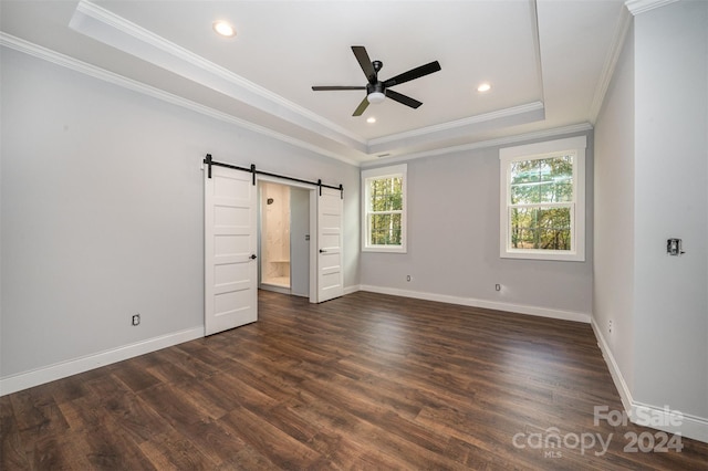 unfurnished bedroom with dark hardwood / wood-style floors, ornamental molding, a barn door, a raised ceiling, and ceiling fan