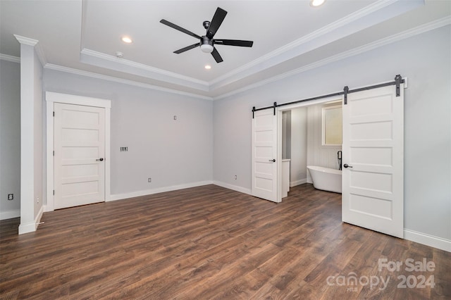 unfurnished bedroom with a barn door, a tray ceiling, ceiling fan, dark wood-type flooring, and ornamental molding