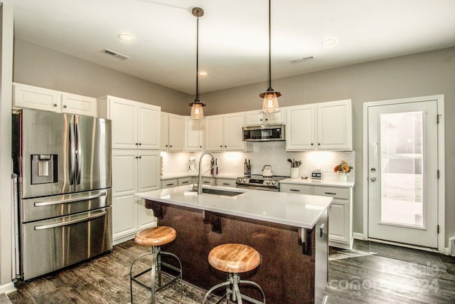 kitchen featuring a center island with sink, decorative light fixtures, stainless steel appliances, and dark hardwood / wood-style flooring