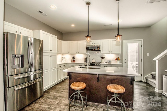 kitchen with appliances with stainless steel finishes, dark hardwood / wood-style flooring, a center island with sink, and a breakfast bar area