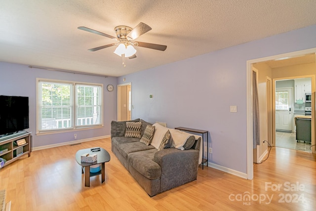 living room featuring ceiling fan, light hardwood / wood-style floors, and a textured ceiling