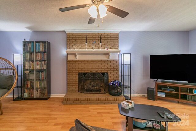 living room featuring ceiling fan, a textured ceiling, light wood-type flooring, and a fireplace