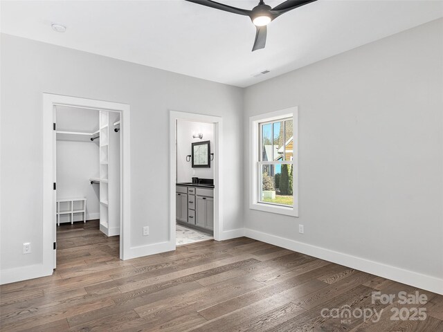 unfurnished bedroom with wood-type flooring, connected bathroom, a spacious closet, and ceiling fan