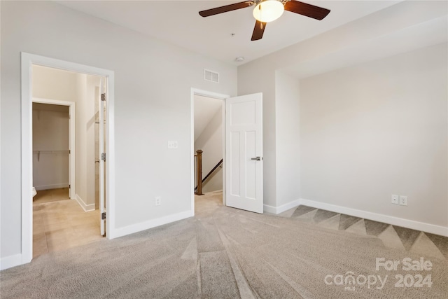 unfurnished bedroom featuring light colored carpet, ceiling fan, a walk in closet, and a closet