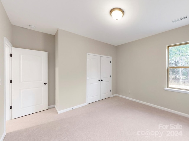 unfurnished bedroom with light colored carpet and a closet