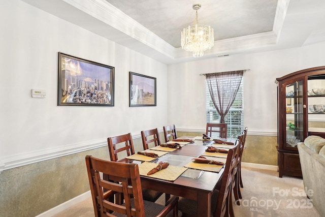 carpeted dining space with a tray ceiling, ornamental molding, and an inviting chandelier