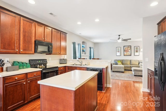 kitchen with black appliances, a center island, sink, kitchen peninsula, and hardwood / wood-style flooring