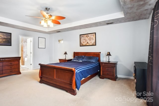 bedroom featuring ceiling fan, ensuite bathroom, a raised ceiling, and light colored carpet