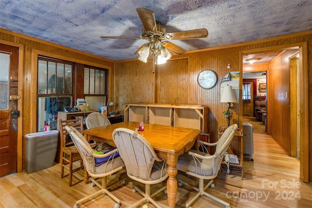 dining area with ceiling fan, a textured ceiling, wooden walls, and light hardwood / wood-style floors