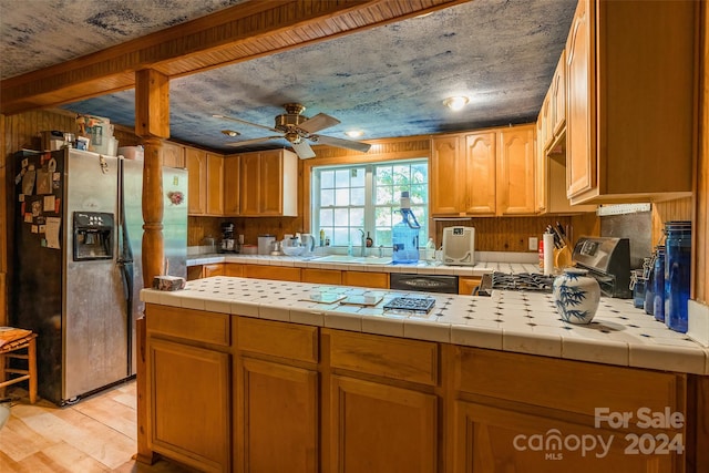 kitchen with ceiling fan, stainless steel fridge, sink, tile counters, and light wood-type flooring