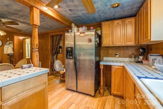 kitchen with stainless steel refrigerator with ice dispenser, wooden walls, and tile countertops