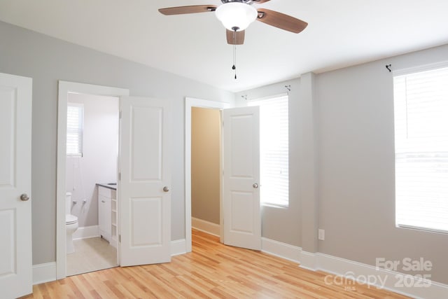 unfurnished bedroom featuring light wood-type flooring, multiple windows, ceiling fan, and connected bathroom