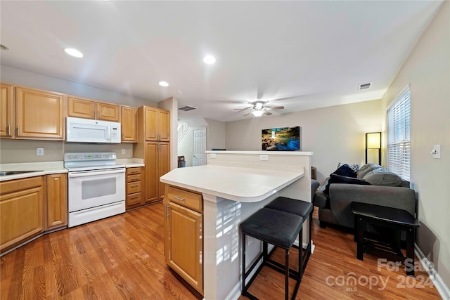 kitchen with ceiling fan, a center island, a breakfast bar, white appliances, and light hardwood / wood-style flooring