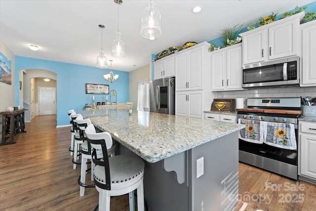 kitchen with pendant lighting, appliances with stainless steel finishes, white cabinetry, an island with sink, and decorative backsplash