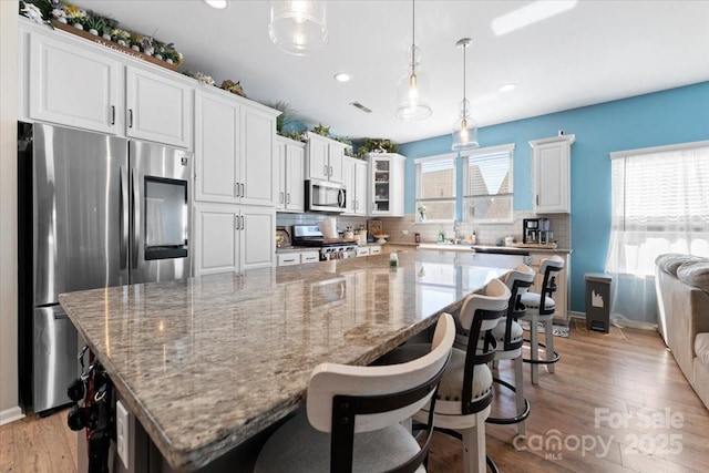 kitchen with appliances with stainless steel finishes, white cabinets, tasteful backsplash, and a large island