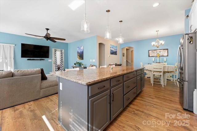 kitchen featuring light hardwood / wood-style flooring, hanging light fixtures, stainless steel fridge, ceiling fan with notable chandelier, and light stone counters