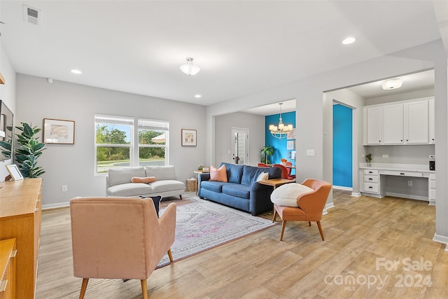 living room with built in desk, an inviting chandelier, and light hardwood / wood-style floors