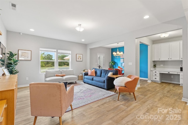 living room featuring an inviting chandelier, built in desk, and light wood-type flooring