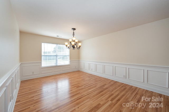 spare room with an inviting chandelier and light hardwood / wood-style flooring