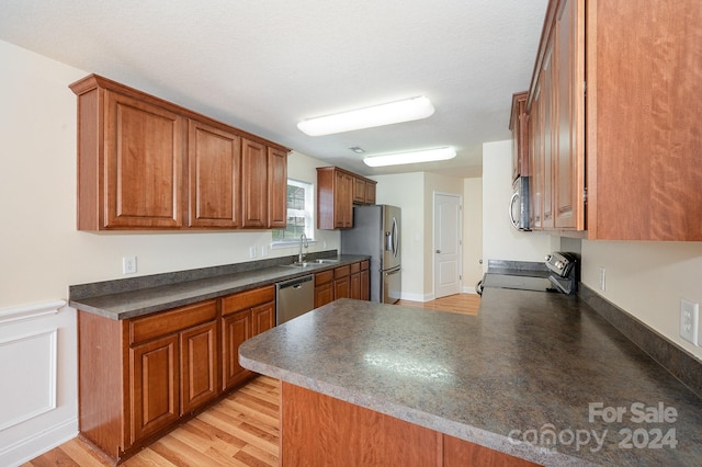 kitchen featuring appliances with stainless steel finishes, light wood-type flooring, kitchen peninsula, and sink