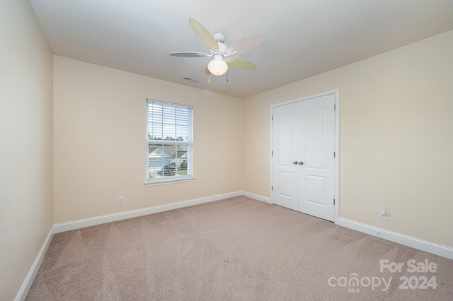 unfurnished bedroom featuring a closet, light colored carpet, and ceiling fan