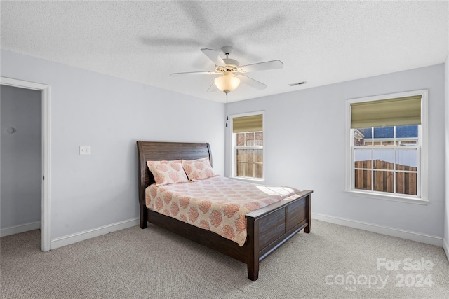 bedroom featuring a textured ceiling, light colored carpet, and ceiling fan