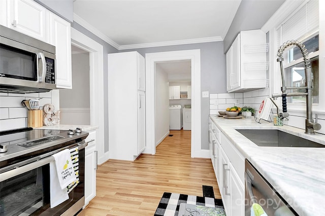 kitchen featuring appliances with stainless steel finishes, tasteful backsplash, washer and dryer, white cabinets, and light hardwood / wood-style floors