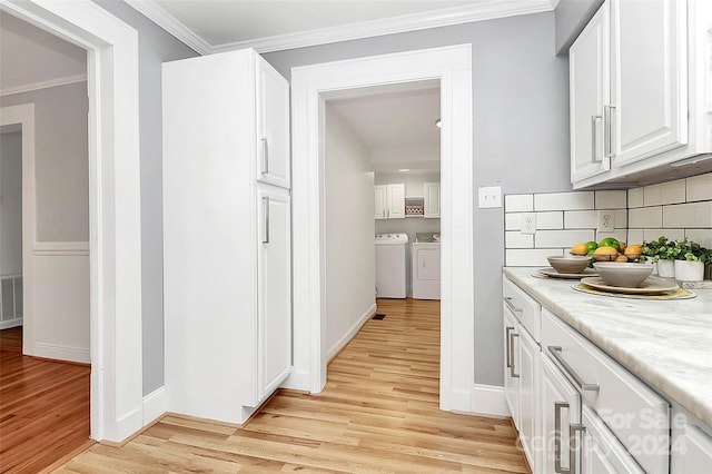 interior space featuring separate washer and dryer, backsplash, light hardwood / wood-style floors, white cabinets, and ornamental molding