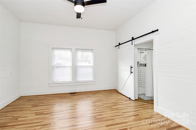 spare room with a barn door, light hardwood / wood-style floors, and ceiling fan