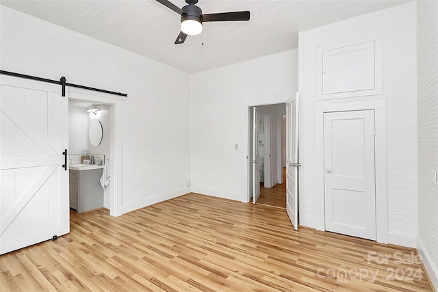 unfurnished bedroom with connected bathroom, a barn door, ceiling fan, and light wood-type flooring