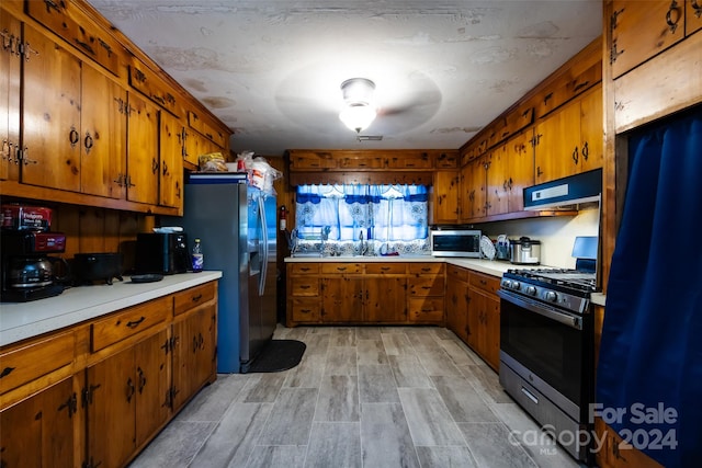 kitchen with light wood-type flooring, sink, stainless steel appliances, and a textured ceiling