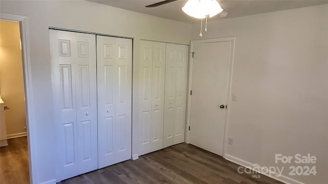 unfurnished bedroom featuring ceiling fan, dark hardwood / wood-style floors, and two closets