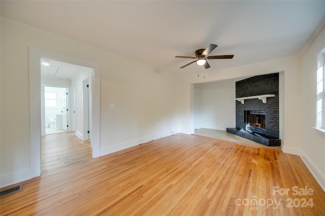 unfurnished living room with ornamental molding, a brick fireplace, ceiling fan, and light hardwood / wood-style flooring