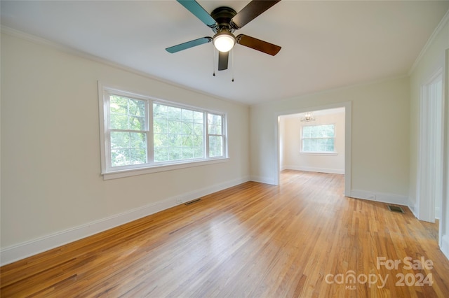 empty room with ceiling fan with notable chandelier, crown molding, and light wood-type flooring