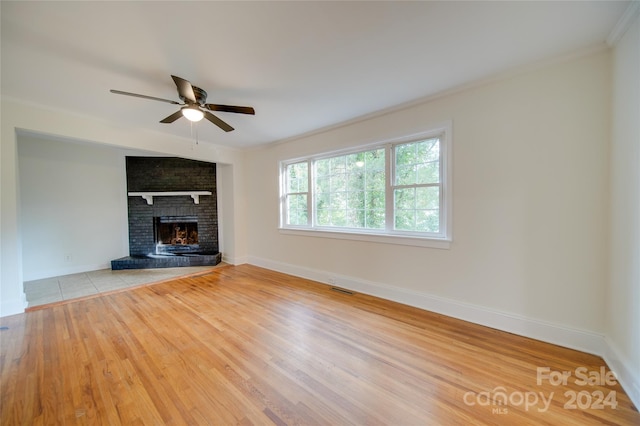 unfurnished living room featuring ornamental molding, light wood-type flooring, ceiling fan, and a brick fireplace