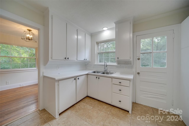 kitchen with light wood-type flooring, decorative light fixtures, sink, ornamental molding, and white cabinetry