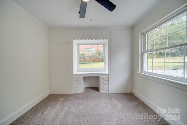 unfurnished bedroom featuring ceiling fan, carpet floors, built in desk, and crown molding