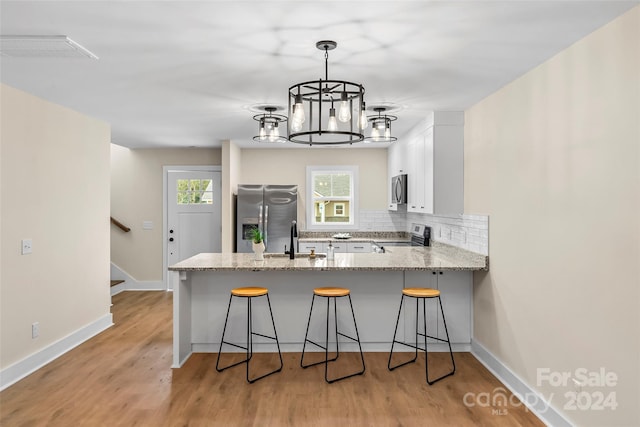 kitchen with appliances with stainless steel finishes, kitchen peninsula, light wood-type flooring, and white cabinets