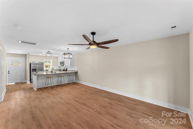 unfurnished living room featuring sink, ceiling fan with notable chandelier, and light hardwood / wood-style floors