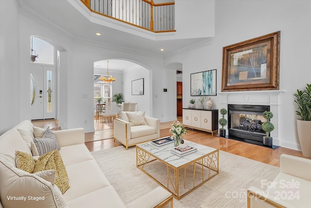 living room featuring a towering ceiling, ornamental molding, hardwood / wood-style floors, and an inviting chandelier