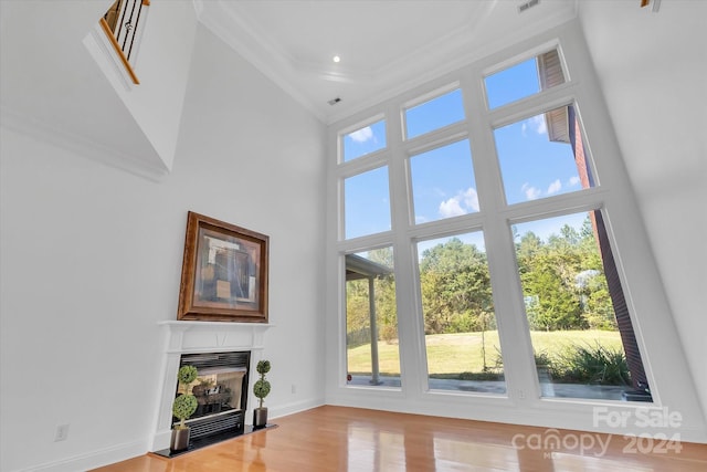 living room with a towering ceiling, ornamental molding, and light hardwood / wood-style flooring